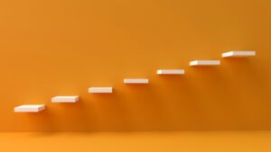 Marches blanches sur fond orange illustrant la progression étape par étape, symbole des petites habitudes qui mènent à de grands résultats.