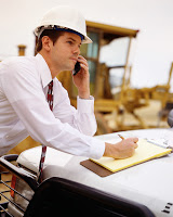 Dirigeant sur un chantier portant un casque de sécurité, avec un portable dans la même gauche et un stylo pour prendre des notes